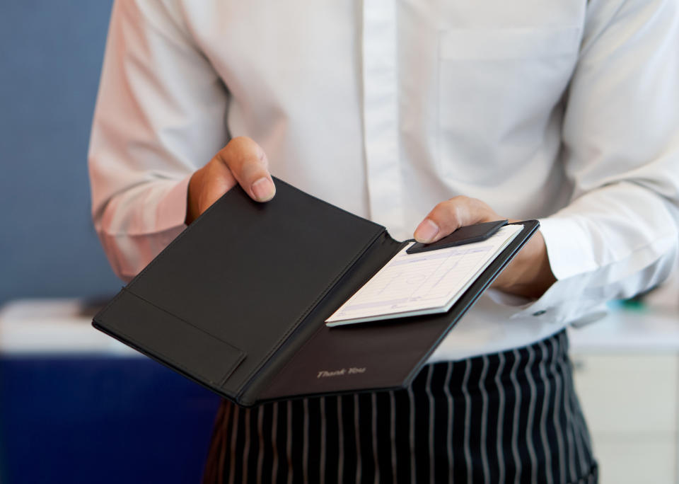 a waiter in a white shirt and apron presents a receipt after calling the bill