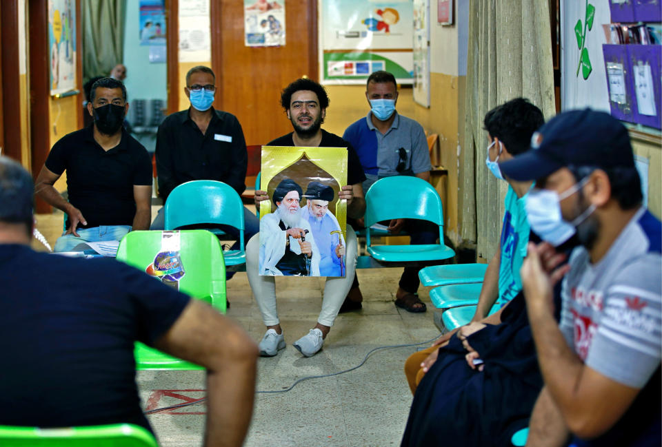 A follower of populist Shiite cleric Muqtada al-Sadr holds a picture of him while waiting with others to receive a dose of the Chinese Sinopharm coronavirus vaccine at a clinic in Sadr City, Baghdad, Iraq, Wednesday, May 4, 2021. Iraq’s vaccine rollout had been faltering for weeks. Apathy, fear and rumors kept many from getting vaccinated despite a serious surge in coronavirus infections and calls by the government for people to register for shots. It took al-Sadr’s public endorsement of vaccinations — and images of him getting the shot — to turn things around. (AP Photo/Hadi Mizban)