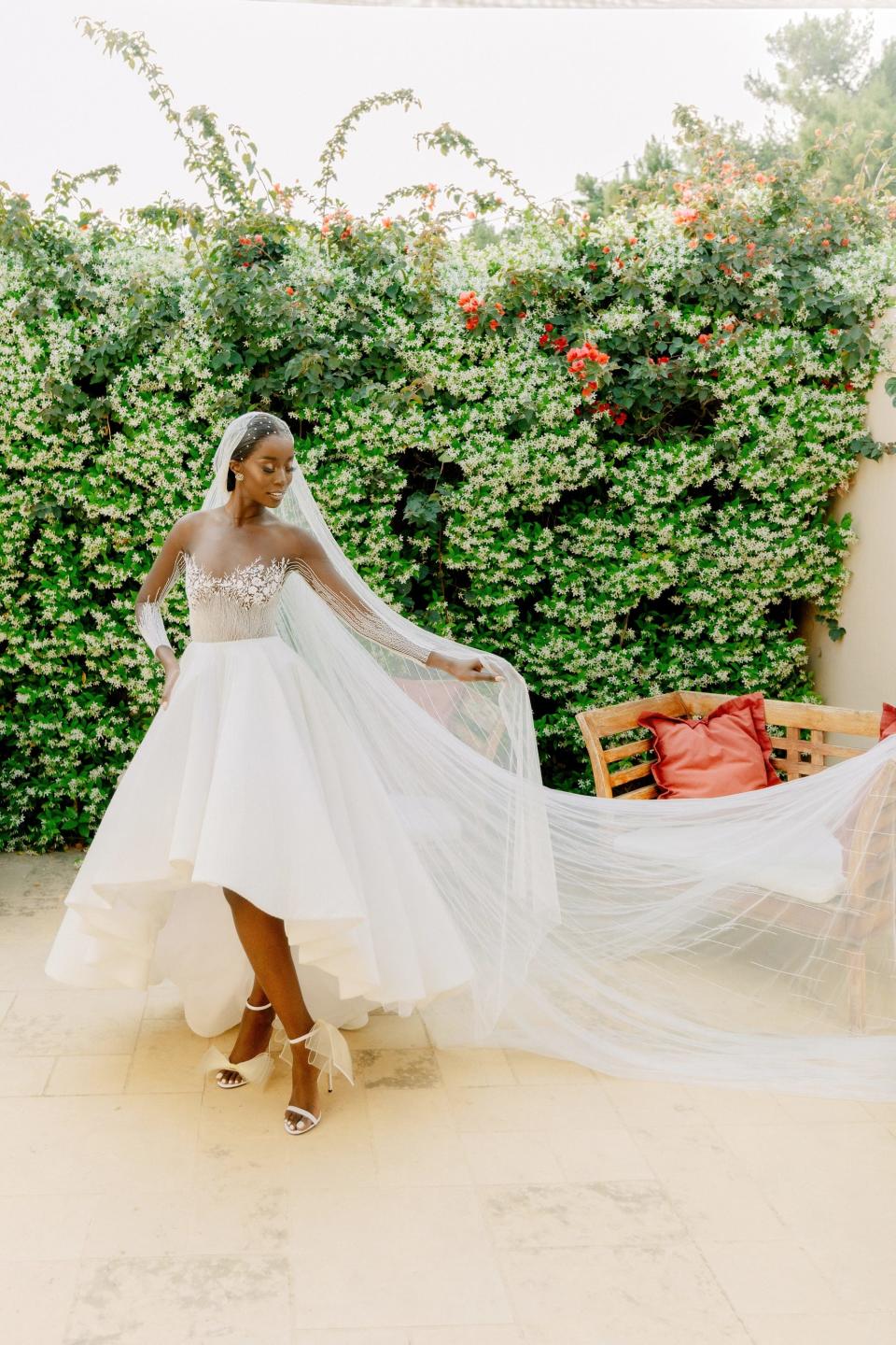 A bride stands in her wedding dress in front of a wall of greenery.