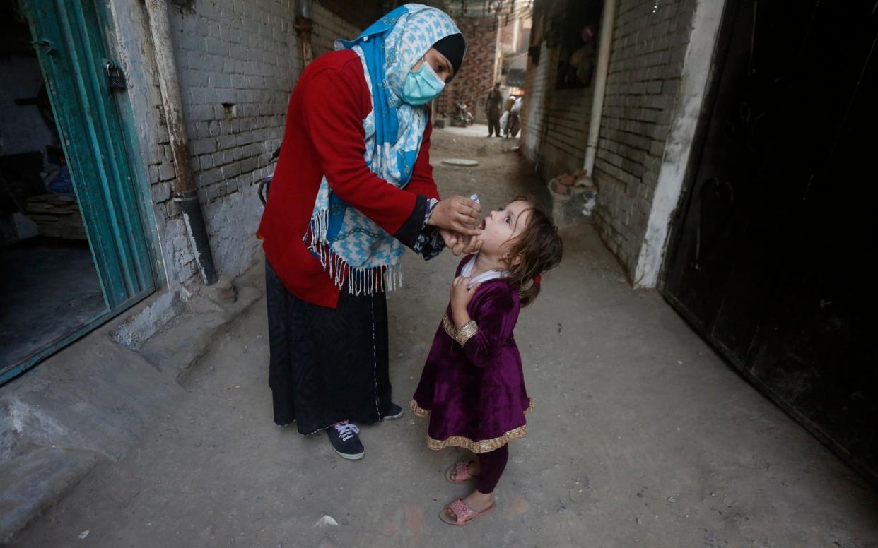 A health worker administers polio vaccine to a girl in Karachi, Pakistan  - KM Chaudary/AP