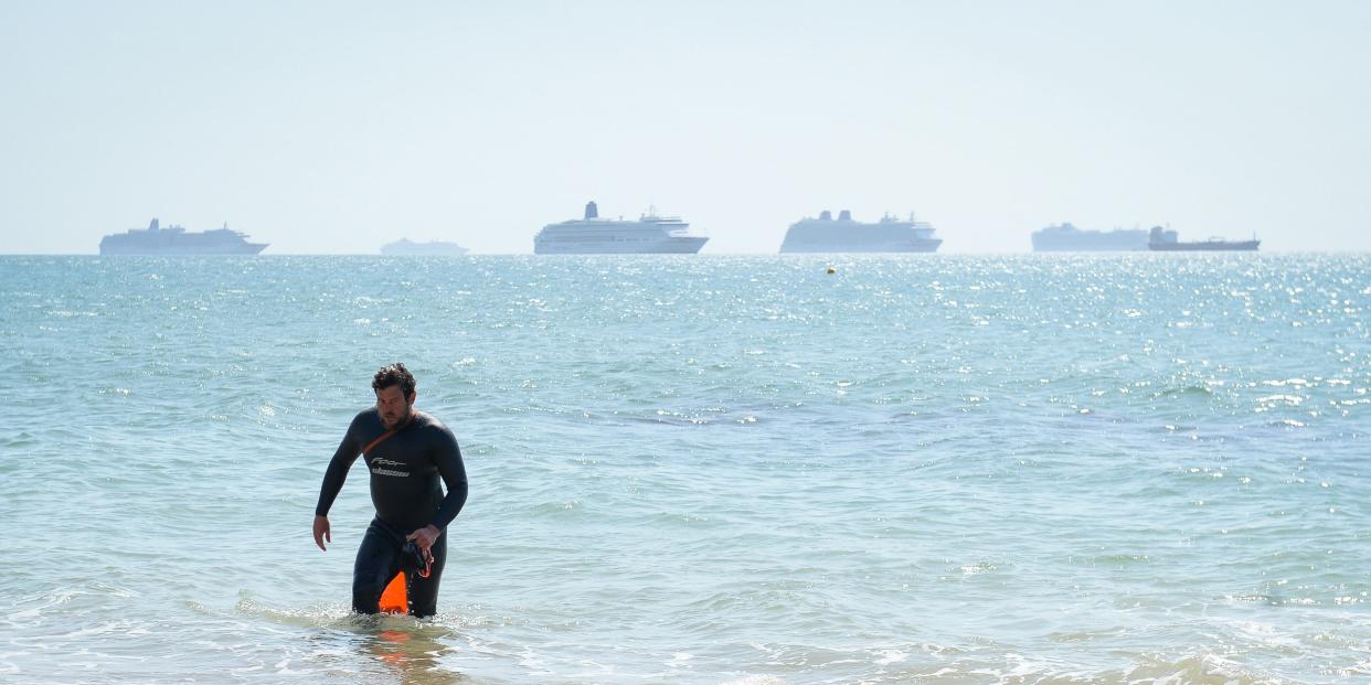 A swimmer exits the sea against the backdrop of a cruise ship off Preston beach on May 24, 2020 in Weymouth, United Kingdom