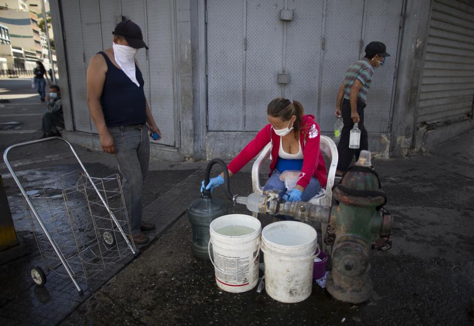 People wearing protective masks as a precaution against the spread of the new coronavirus collect water from a hydrant, in Caracas, Venezuela, Tuesday, March 17, 2020. President Nicolas Maduro ordered citizens to stay home, and to wear a mask when in public. The vast majority of people recover from the new virus. (AP Photo/Ariana Cubillos)