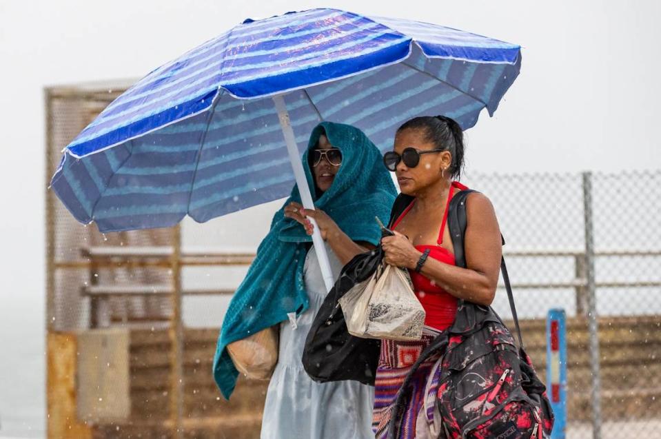 Melida Ortega, left, and Etna Solis hold an umbrella and walk toward their car as lightning and heavy rain falls over Hobie Island Beach Park on Monday, June 19, 2023, in Miami, Fla.