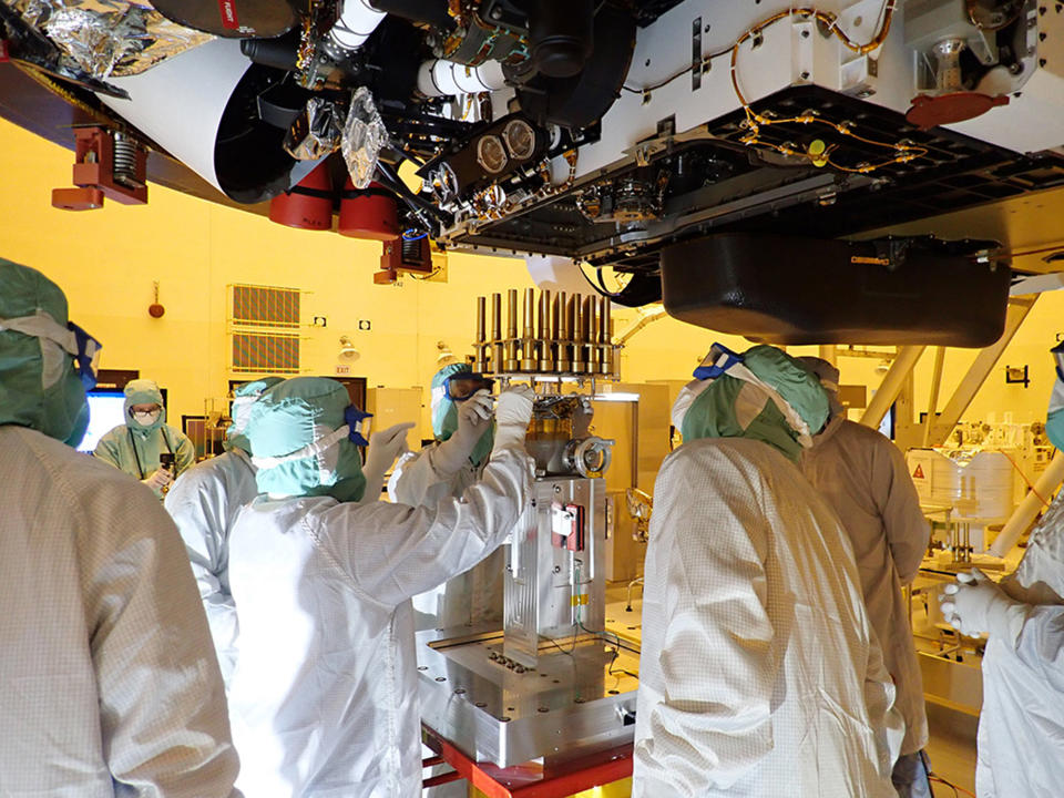 In this May 20, 2020 photo made available by NASA/JPL-Caltech, engineers and technicians insert sample tubes into the belly of the Perseverance Mars rover at the Kennedy Space Center in Florida. NASA is upping the ante with its newest rover headed to Mars. Set to rocket away this week from Florida, Perseverance is NASA's brawniest and brainiest Martian rover yet. (NASA/JPL-Caltech via AP)