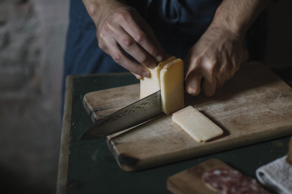 A person cutting into a block of cheese on a wood cutting board. 