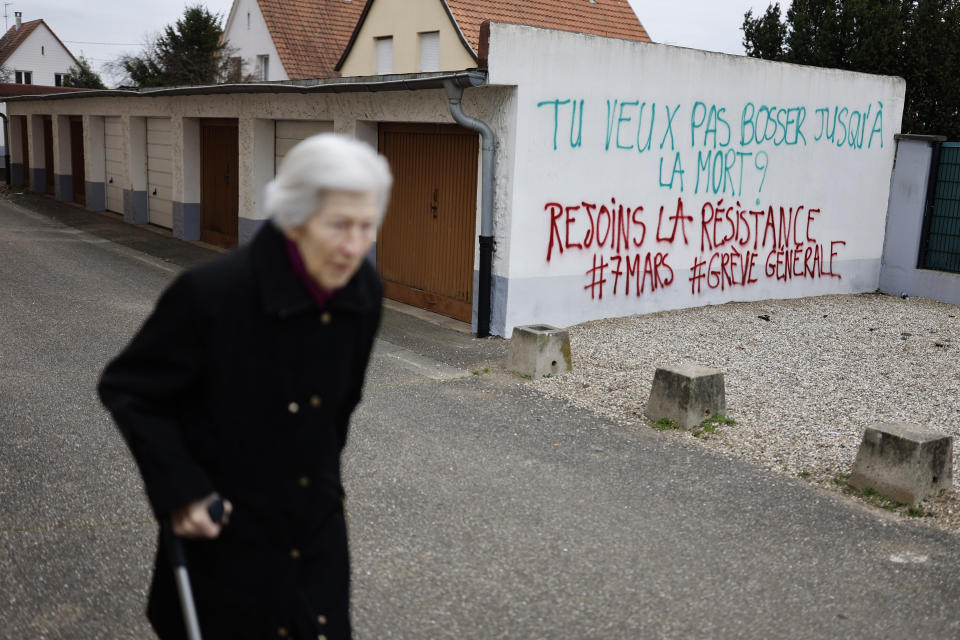 An elderly woman walks past graffitis reading"You want to work until death? Join resistance, General Strike on March 7" in Strasbourg eastern France, Sunday, March 5, 2023. The government is bracing for the biggest disruptions Tuesday, March 7, 2023 when strikes are expected across multiple sectors and protests are planned in cities across France against the retirement bill. The reform, which would raise the official pension age from 62 to 64 (AP Photo/Jean-Francois Badias)