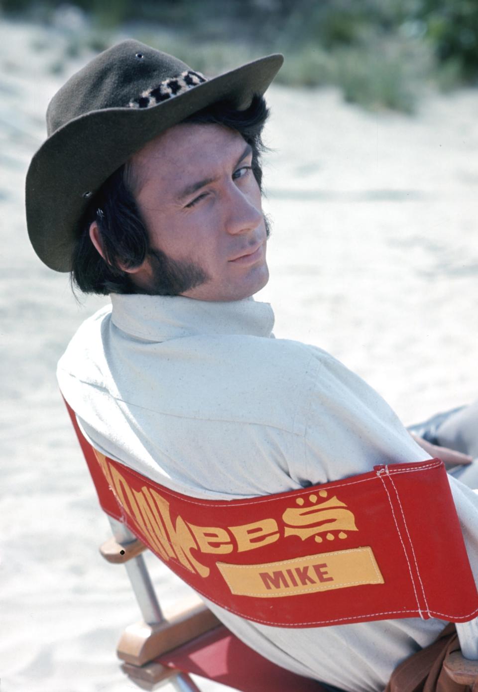 Michael Nesmith in a hat and sitting on a chair