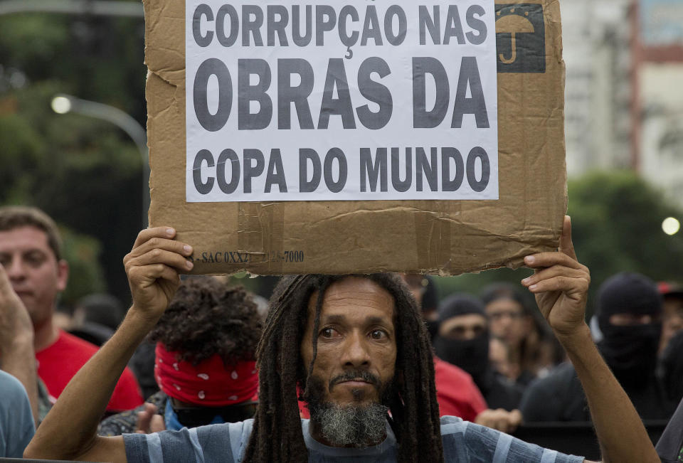 A demonstrator holds a banner made from cardboard with a message that reads in Portuguese; "Corruption on the constructions of the World Cup," during a protest against the upcoming World Cup soccer tournament in Sao Paulo, Brazil, Saturday, Feb. 22, 2014. Hundreds of protesters gathered demonstrating against the billions of dollars being spent to host this year's World Cup while the nation's public services remain in a woeful state. The protest started peacefully, but adherents to the Black Block anarchist tactics vandalized banks and clashed with police, who used tear gas and stun grenades to disperse the violent demonstrators. (AP Photo/Andre Penner)