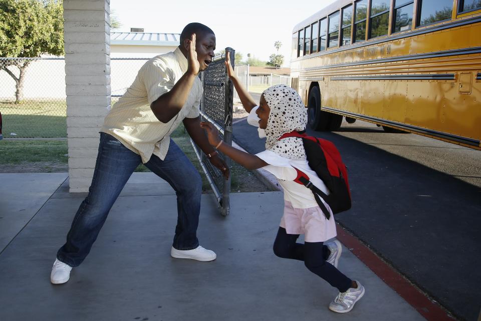 Samuel Lavi, left, a Congolese native who is a teaching assistant and family engagement liaison, greets first grader Kediga Ahmed as she arrives at the Valencia Newcomer School attend class Thursday, Oct. 17, 2019, in Phoenix. Children from around the world are learning the English skills and American classroom customs they need to succeed at so-called newcomer schools. Valencia Newcomer School in Phoenix is among a handful of such public schools in the United States dedicated exclusively to helping some of the thousands of children who arrive in the country annually. (AP Photo/Ross D. Franklin)