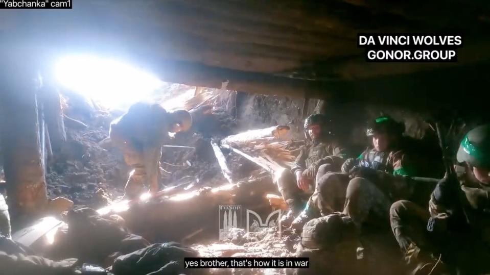 Bodycam footage shows four soldiers crouched in a rudimentary dugout made of earth and wood.