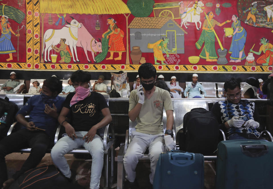 Indian passengers wear face masks and gloves as a precaution against COVID-19 wait at Secunderabad Railway Station in Hyderabad, India, Saturday, March 21, 2020. For most people, the new coronavirus causes only mild or moderate symptoms. For some it can cause more severe illness. (AP Photo/Mahesh Kumar A.)