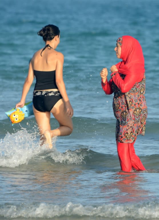 Tunisian women, one (R) wearing a "burkini", a full-body swimsuit designed for Muslim women, pictured at Ghar El Melh beach near Bizerte, northeast of the capital Tunis, on August 16, 2016