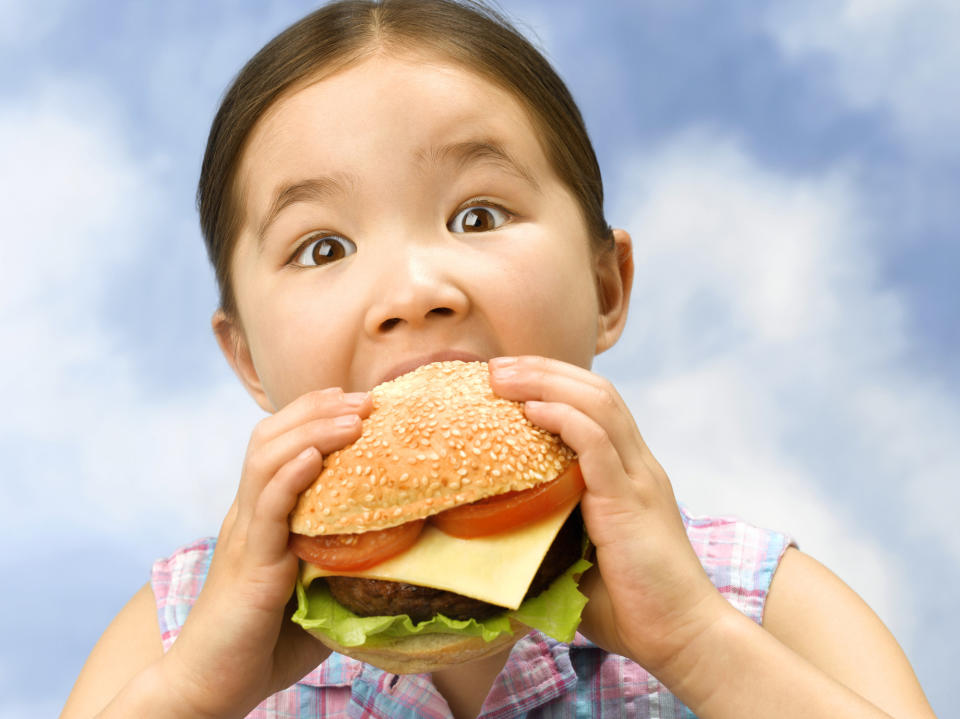 Little girl taking a bit of a big burger