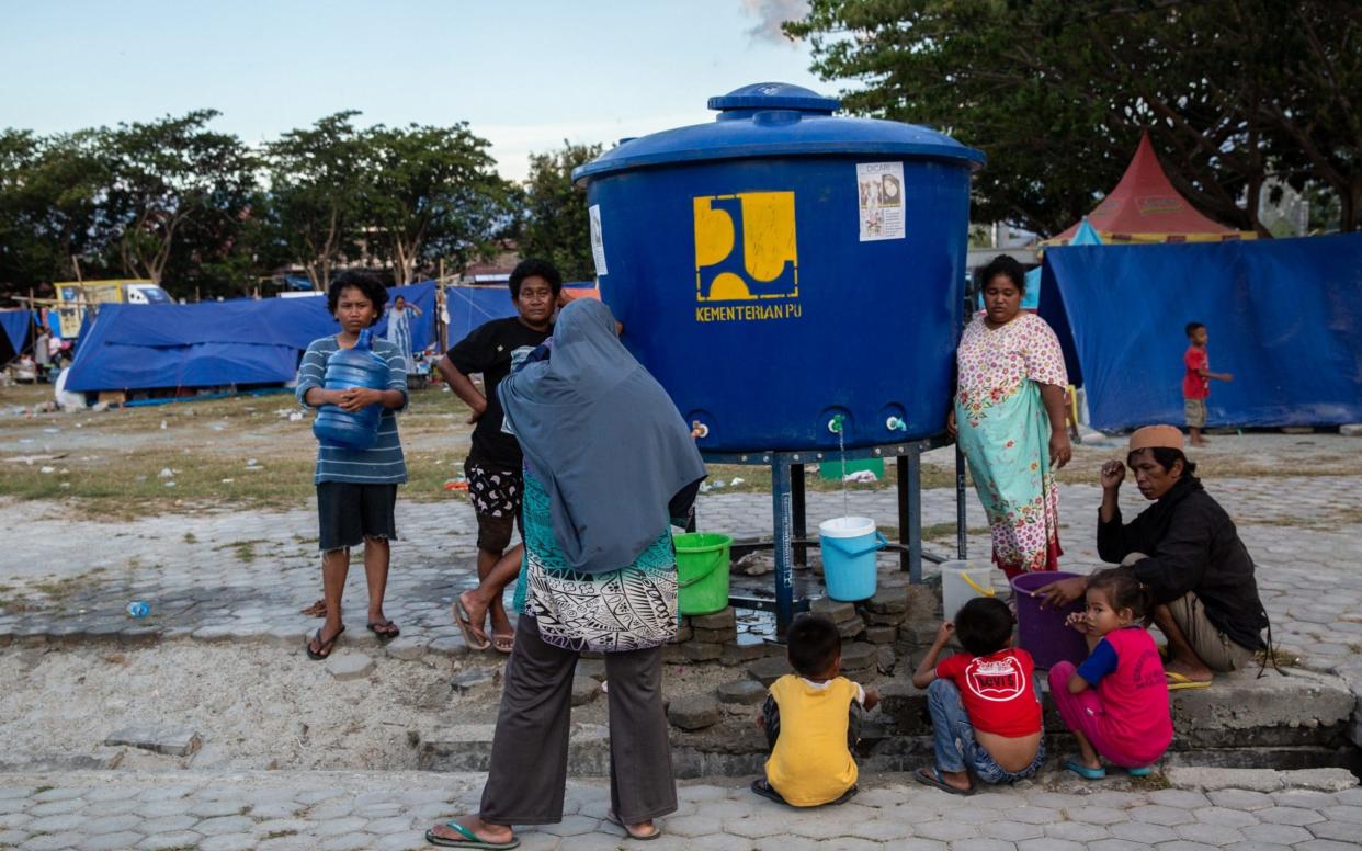 People get water from a tank at a temporary shelter in Palu - Bloomberg