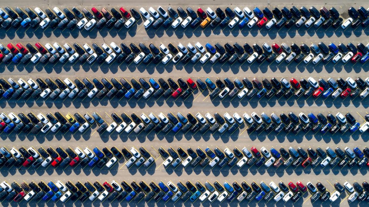 Aerial view of new cars of different brands parked in rows on a lot.