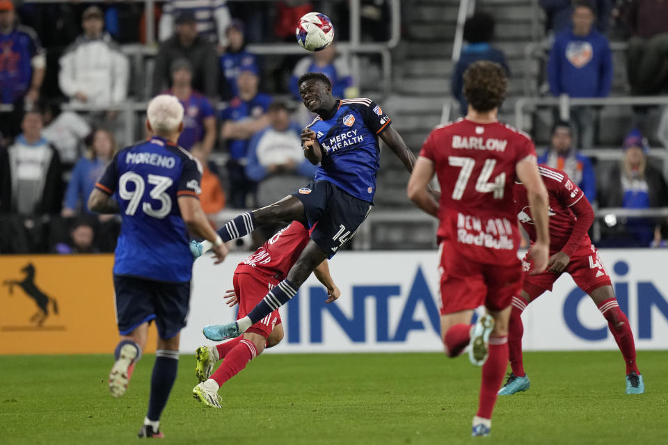 FC Cincinnati forward Dominique Badji (14) heads the ball as FC Cincinnati midfielder Júnior Moreno (93) and New York Red Bulls forward Tom Barlow (74) move in during the first half of an MLS playoff soccer match in Cincinnati, Sunday, Oct. 29, 2023. (AP Photo/Carolyn Kaster)