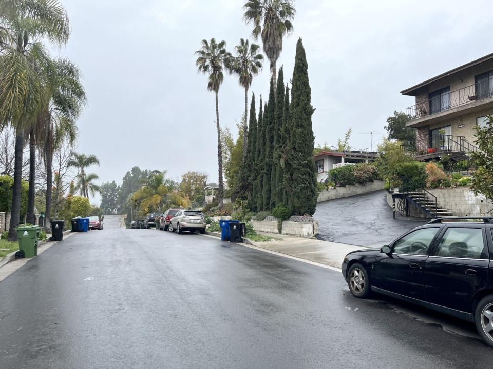 Cars and trash bins are on a street in Highland Park