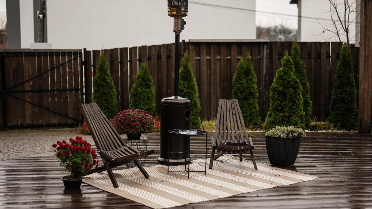 stainless steel metal gas outdoor patio heater with wooden chairs and pot with flowers at wet terrace place to relax