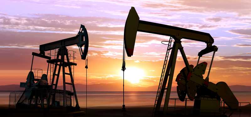 Two oil pumpjacks operating with sun setting in the background.