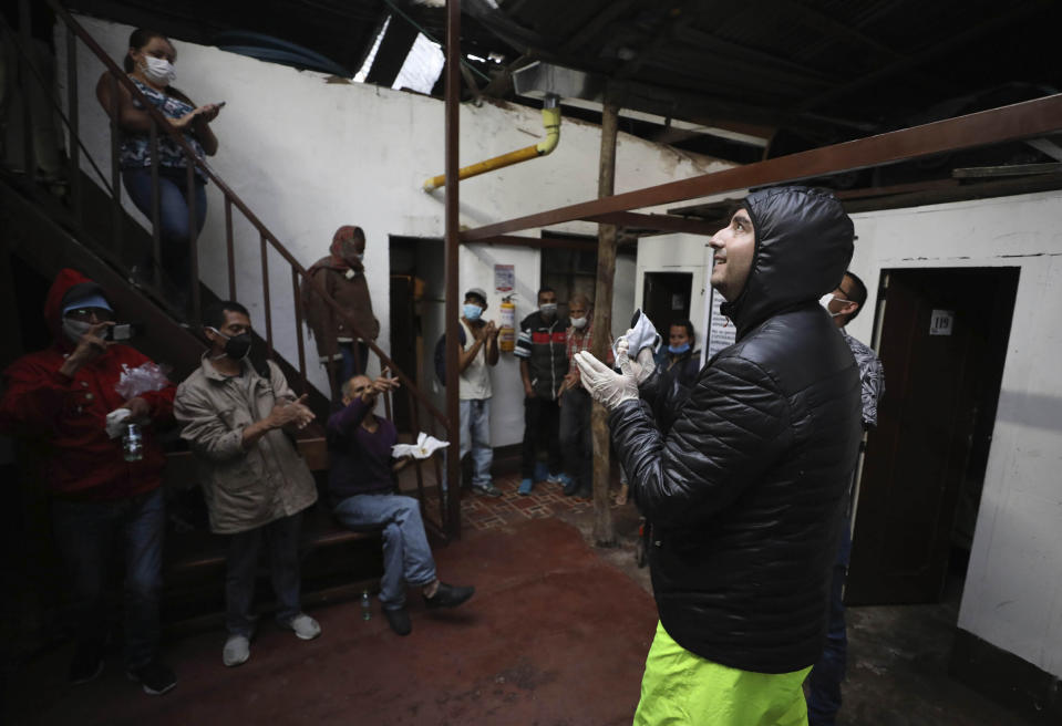 FILE - In this March 30, 2020 file photo, Emiliano Moscoso, right, talks to Venezuelan and Colombian people in a boarding house in Bogota, Colombia. Moscoso recently launched a program called Solidarity Menu to feed people in need during the coronavirus outbreak. (AP Photo/Fernando Vergara, File)