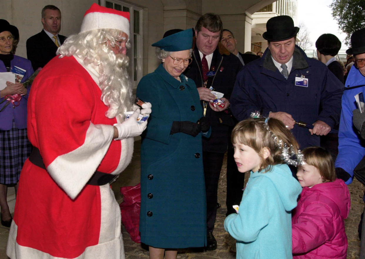 Britain's Queen Elizabeth II helps Santa Claus to hand out gifts to child racegoers at Ascot.   (Photo by Fiona Hanson - PA Images/PA Images via Getty Images)