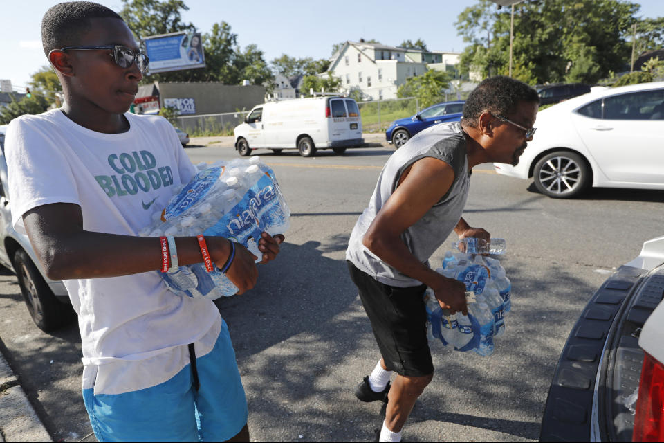 FILE- In this Aug. 12, 2019 file photo, volunteer Matthew Tiggs, left, helps Newark resident Mack Mayton load cases of bottled water into the trunk of his car in Newark, N.J., after Mayton picked it up at the Boylan Street Recreation Center. New Jersey's biggest city has recently been the epicenter of a problem with lead in drinking water, but the United States has an estimated 6 million lead pipes, many of them in unknown locations. (AP Photo/Kathy Willens, File)