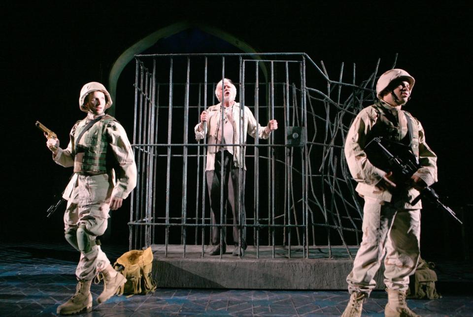 A man stands behind bars, guarded by two soldiers, in a scene from Rajiv Joseph's "Bengal Tiger at the Baghdad Zoo."