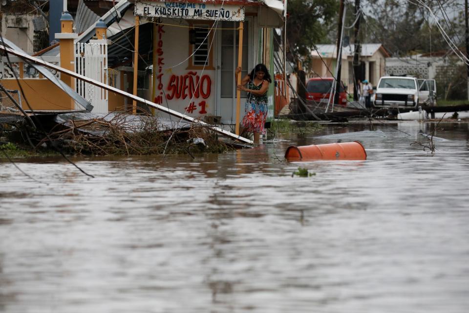 a woman holds on to a wooden pillar surrounded by floodwaters from hurricane maria