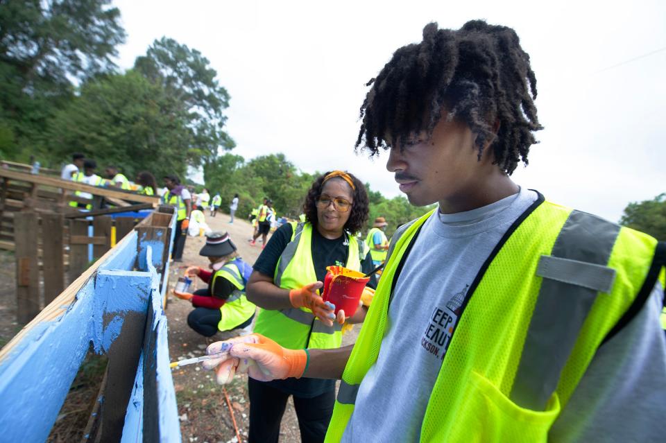 Mario Speech, foreground, a Capital City Alternative School student, helps to beautify Percy V. Simpson Drive as he works on a mural during a Jackson Citywide Day of Service Monday, Aug. 28, 2023. The trash buildup from dumping on Simpson Drive prevented anyone from using the road. With debris cleared, murals were painted on pallets that had been dumped.