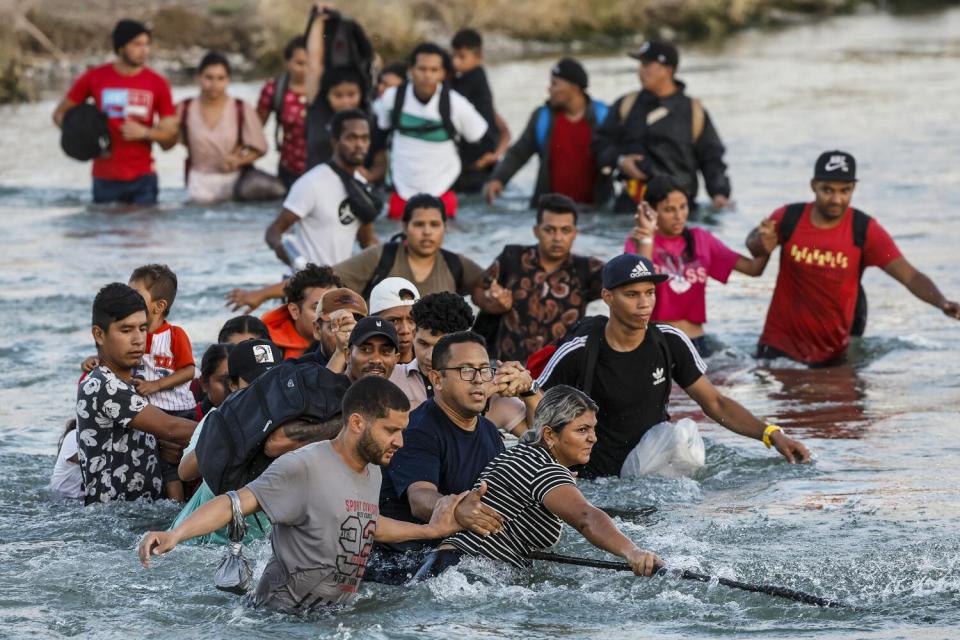 A large group of people hold on to each other in waist-deep water.