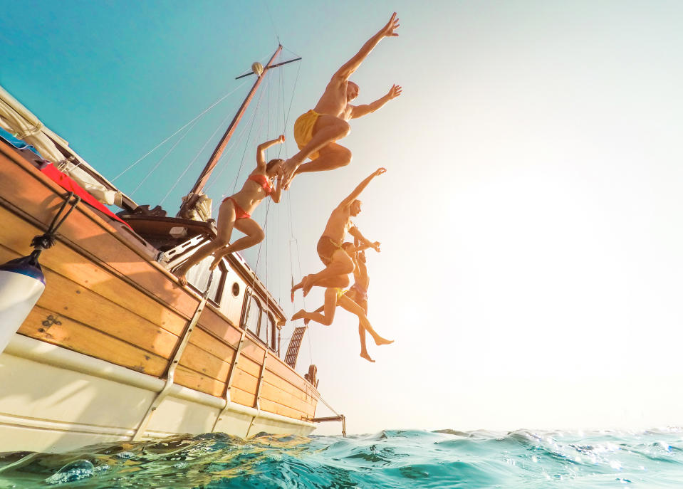 Young people jumping inside ocean in summer excursion day - Happy friends diving from sailing boat into the sea - Vacation, youth and fun concept - Focus on bodies silhouette - Fisheye lens distortion