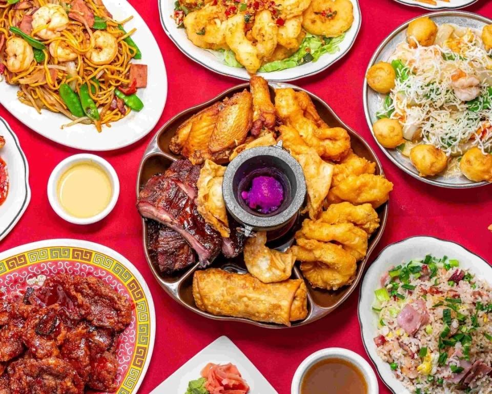 Assorted Chinese dishes on plates, including ribs, fried rice, noodles, egg rolls, and battered shrimp, arranged around a circular serving tray