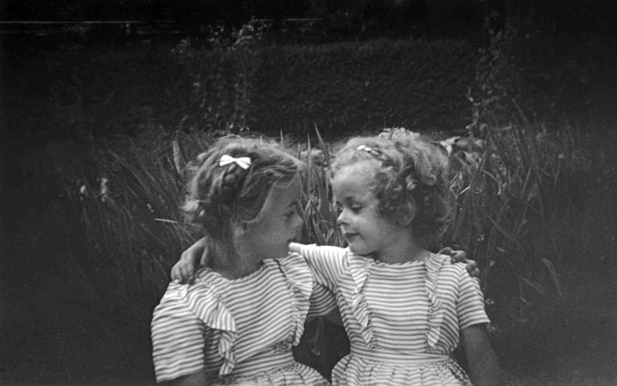 Sisters in their identical striped summer dresses, embracing in the garden.