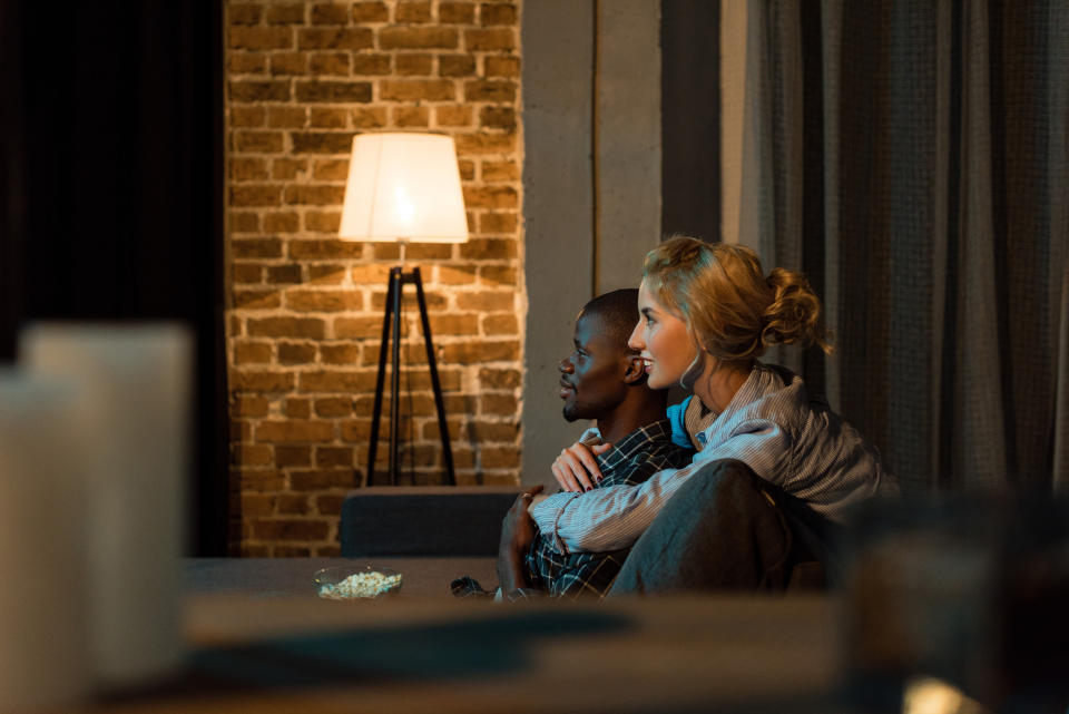 A couple watching TV with a bright lap against a brick wall in the background.