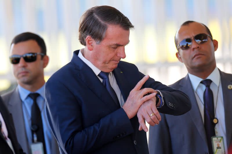 Brazil's President Jair Bolsonaro looks at his watch while meeting supporters as he leaves Alvorada Palace, amid coronavirus disease (COVID-19) outbreak, in Brasilia