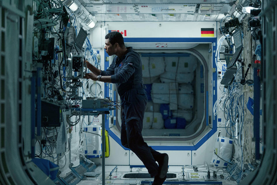 a man in a blue flight stands in a white hallway with many wires and other equipment on the walls