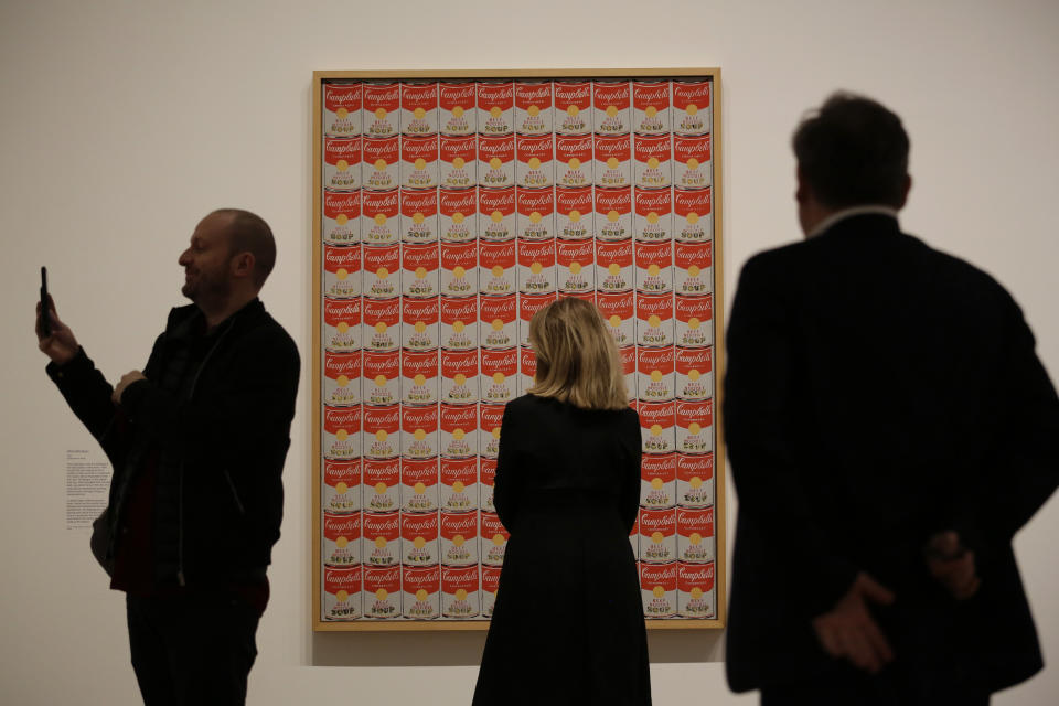 A Tate representative, center, poses for photographs next to the Andy Warhol 1962 piece "100 Campbell's Soup Cans" during a media preview for the exhibition "Andy Warhol" at the Tate Modern gallery in London, Tuesday, March 10, 2020. The exhibition, which runs from March 12 to September 6, features over 100 works spanning the American artist's career in the second half of the 20th century until his death in 1987. (AP Photo/Matt Dunham)