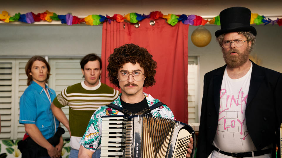 A man with a mustache and glasses solemnly playing accordion at a party with several people behind him; still from "WEIRD: The Al Yankovic Story"