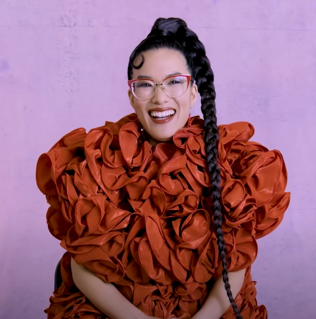 Ali Wong laughs during an interview with the Hollywood Reporter. She's wearing a voluminous ruffled dress and her hair is styled into an ultra long single braid