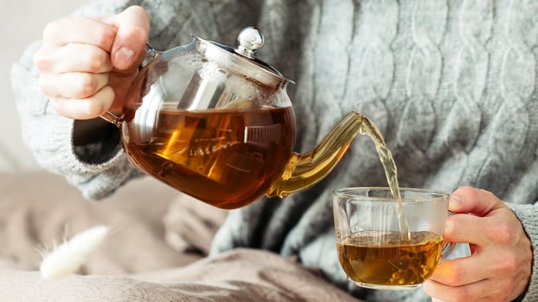 Person pouring tea from glass teapot