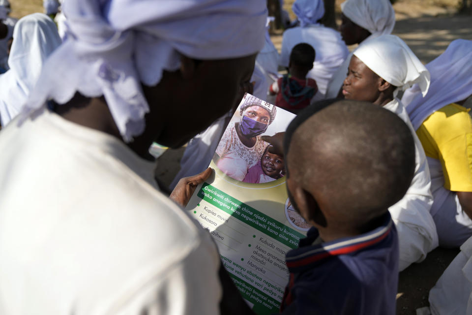 A woman member of the apostolic church reads a measles vaccination flier with her baby while attending church in the impoverished Epworth region outside Harare, Friday, Sept. 16, 2022. Church members in Zimbabwe are getting their children vaccinated against measles in secret amid a deadly outbreak. It's to avoid being shunned by religious leaders who are opposed to modern medicine. (AP Photo/Tsvangirayi Mukwazhi)