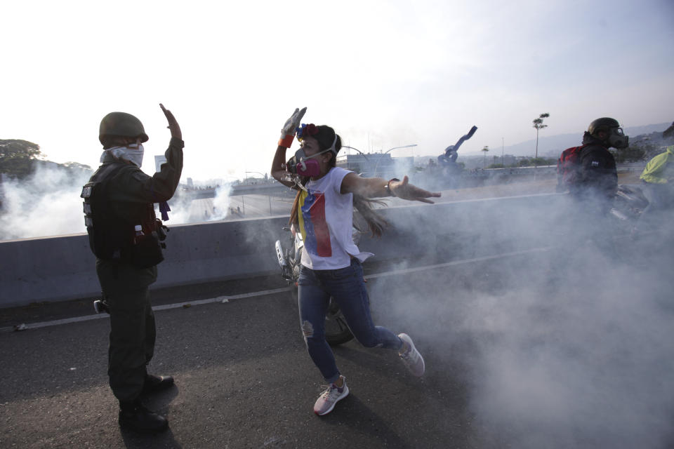 Un opositor al presidente venezolano Nicolás Maduro saluda a un soldado rebelde en el paso elevado de una carretera en las afueras de la base aérea de La Carlota, en medio de gases lacrimógenos disparados por soldados leales dentro de la base en Caracas, el martes 30 de abril de 2019. (Foto AP/Boris Vergara)