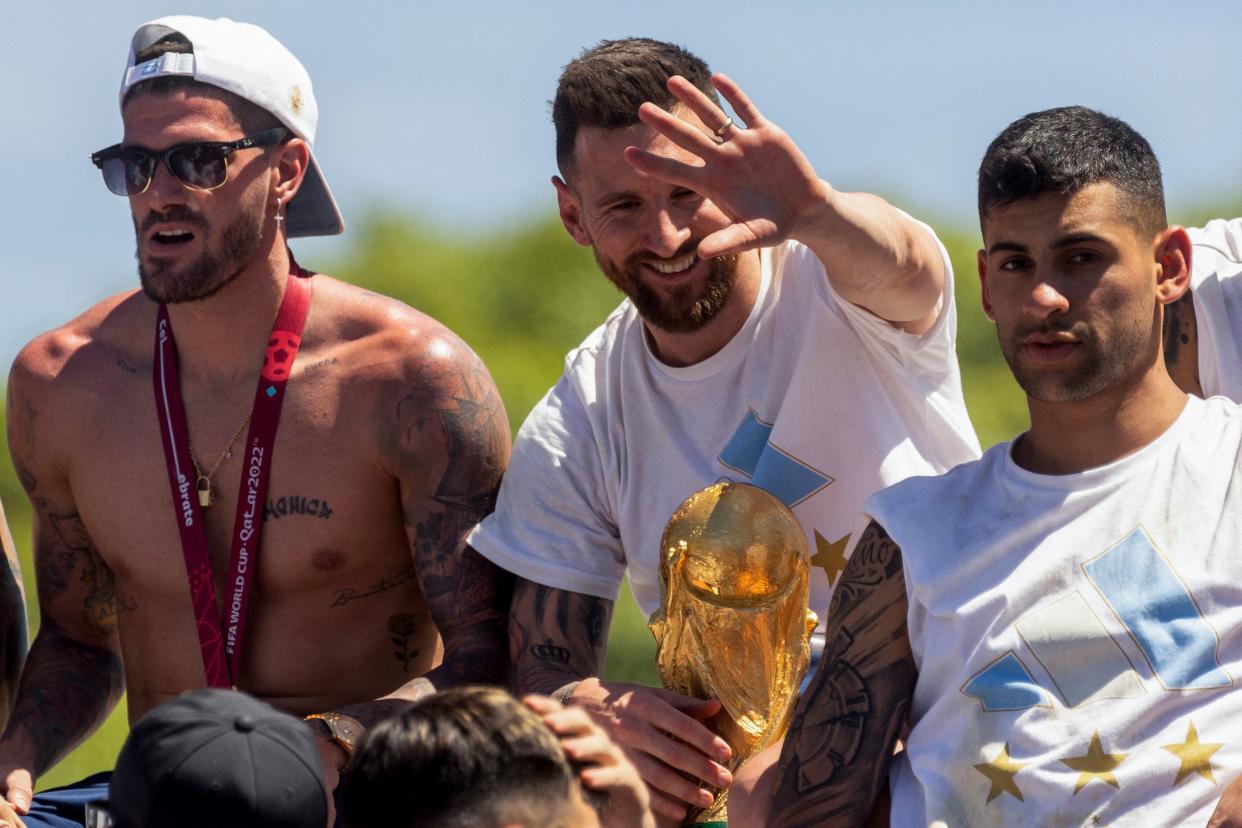 Argentine players Rodrigo De Paul (L), Lionel Messi (C) and Cristian Romero (R) celebrate on board a bus with a sign reading 