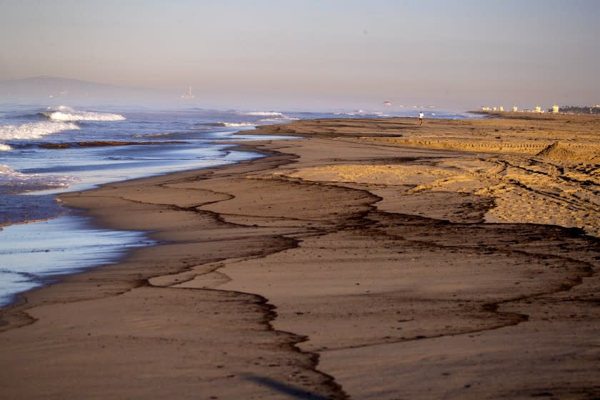 Huntington Beach, CA - October 03: An oil slick lines the beach as a man walks, taking in the scene of a major oil spill washing ashore at Huntington State Beach in Huntington Beach Sunday, Oct. 3, 2021. Crews raced Sunday morning to contain the damage from a major oil spill off the Orange County coast that left crude spoiling beaches, killing fish and birds and threatening local wetlands. The oil slick is believed to have originated from a pipeline leak, pouring 126,000 gallons into the coastal waters and seeping into the Talbert Marsh as lifeguards deployed floating barriers known as booms to try to stop further incursion, said Jennifer Carey, Huntington Beach city spokesperson. At sunrise Sunday, oil was on the sand in some parts of Huntington Beach with slicks visible in the ocean as well. "We classify this as a major spill, and it is a high priority to us to mitigate any environmental concerns," Carey said. "It's all hands on deck." (Allen J. Schaben / Los Angeles Times)