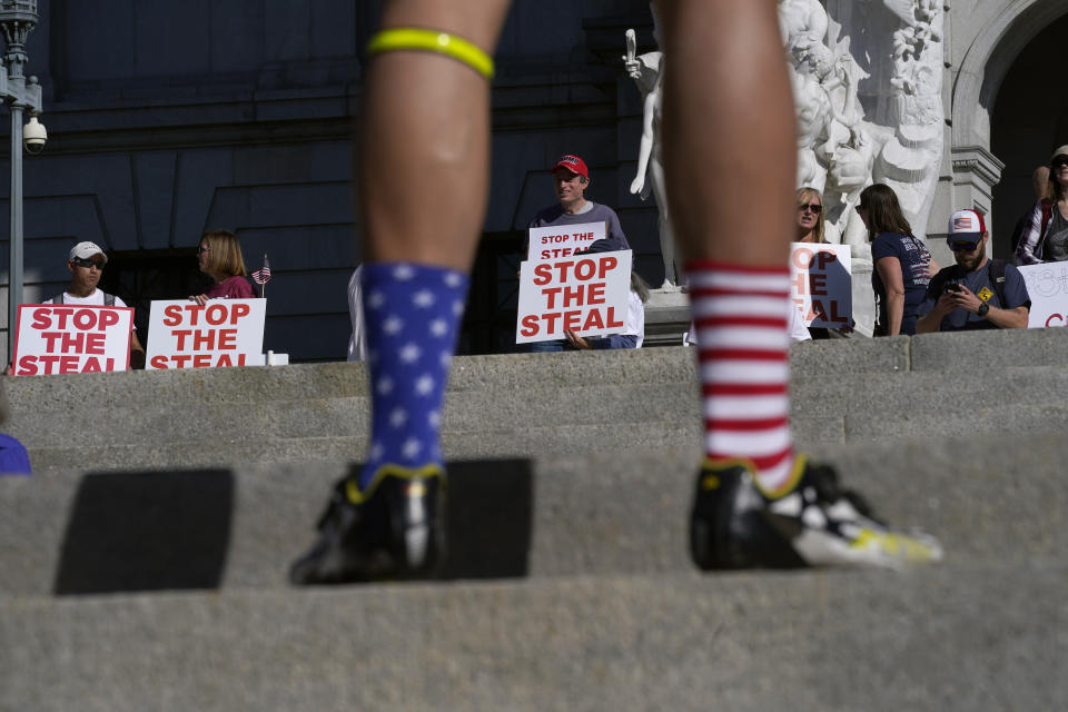 A supporter of President Donald Trump wears red, white and blue socks as he speaks with demonstrators, rear, outside the Pennsylvania State Capitol, Friday, Nov. 6, 2020, in Harrisburg, Pa., as vote counting continues following Tuesday's election. (AP Photo/Julio Cortez)