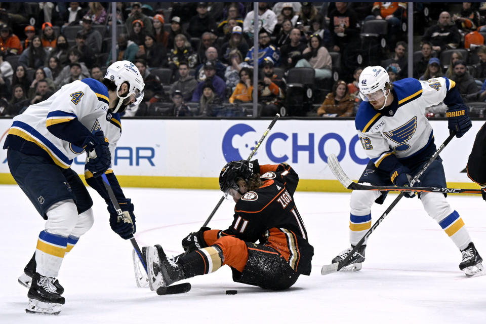 Anaheim Ducks center Trevor Zegras, center, attempts to pass the puck while seated on the ice between St. Louis Blues defenseman Nick Leddy, left, and right wing Kasperi Kapanen during the second period of an NHL hockey game in Anaheim, Calif., Saturday, March 25, 2023. (AP Photo/Alex Gallardo)