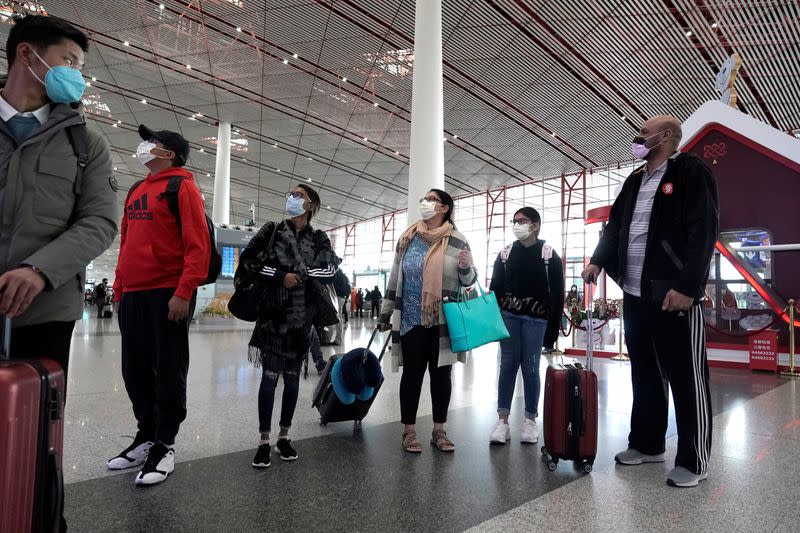Foreign travellers wearing masks check their flight's departure information at Beijing International Airport in Beijing