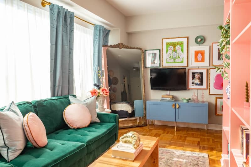 A living room with a green fabric couch across from a pink bookcase and gallery wall