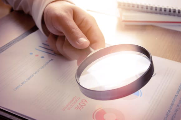 A person holding a magnifying glass up to financial reports.