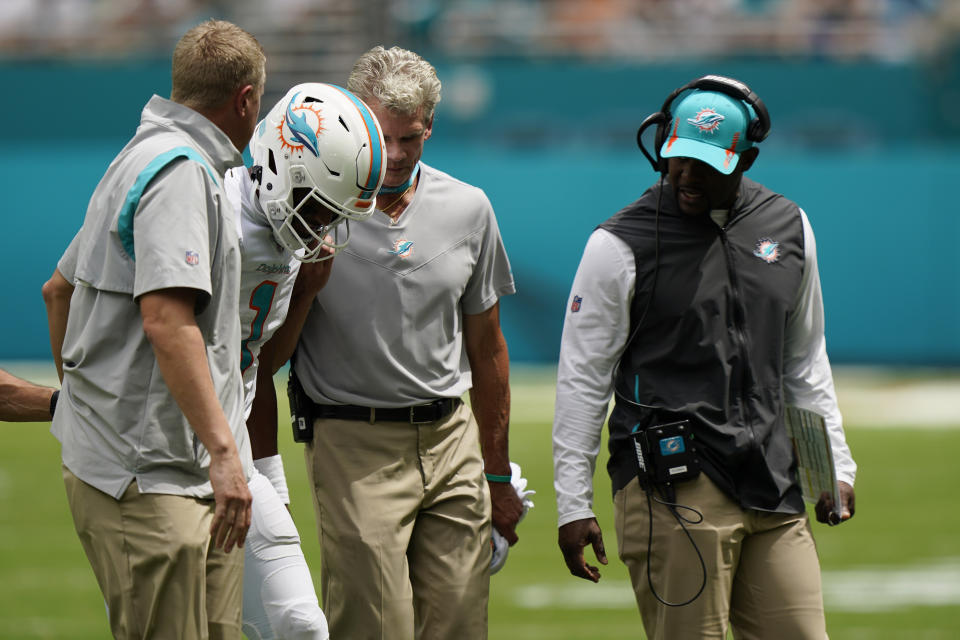 Miami Dolphins quarterback Tua Tagovailoa (1) is helped off the field after being injured, as Miami Dolphins head coach Brian Flores, right, looks on, during the first half of an NFL football game, Sunday, Sept. 19, 2021, in Miami Gardens, Fla. (AP Photo/Wilfredo Lee)